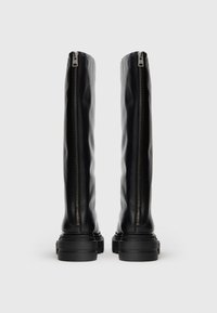 Botas de cuero negro hasta la rodilla con cremalleras laterales dobles y suelas gruesas, con una textura suave y un diseño minimalista.