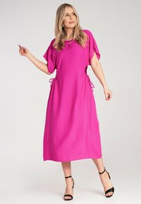 Rosa Midikleid mit kurzen Ärmeln, Bindedetails an der Taille, aus leichtem Stoff, ergänzt durch schwarze Riemchensandalen.