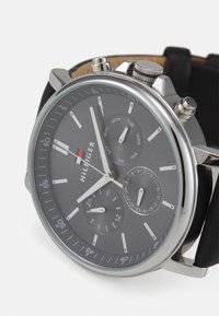 Montre en acier inoxydable argenté avec un cadran gris, trois sous-cadrans et un bracelet en cuir noir. Comprend des marqueurs d'heure et un affichage de la date.