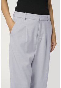 Jasnofioletowe spodnie wykonane z gładkiego materiału, charakteryzujące się dopasowanym krojem, plisami i bocznymi kieszeniami, z płaskim pasem w talii.