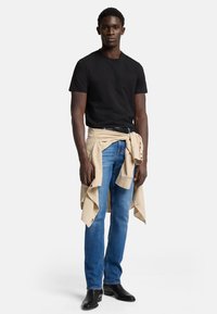 Czarny t-shirt z krótkim rękawem, beżowa koszula związana w talii, niebieskie dżinsy i czarne botki za kostkę. Prosty, czysty design.