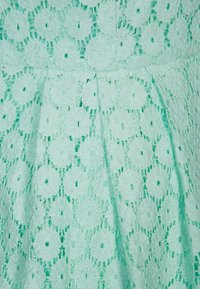 Myntgrön spets tyg med ett blommönster med cirkulära motiv, arrangerade i en rutnätsdesign. Texturerat utseende med en mjuk finish.