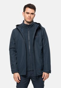 Marineblauwe waterdichte jas met capuchon, met een rits aan de voorkant en een fleece binnenlaag. Glad textuur, minimale branding en verstelbare manchetten.