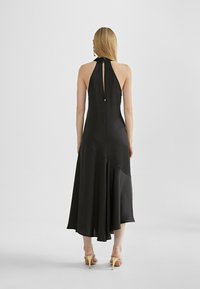 Black halter-neck dress with a fitted bodice, flowing skirt, and asymmetrical hem. Features a keyhole back and minimal embellishments.