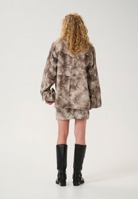 Smeđi tie-dye oversized majica s leđnim jaram, u paru s odgovarajućom suknjom. Model nosi crne kožne čizme do koljena.