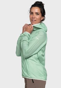 Leichte mintgrüne Jacke mit Kapuze, aus einem glatten, wasserabweisenden Stoff gefertigt. Auffällige weiße Akzente an den Nähten und Bündchen.