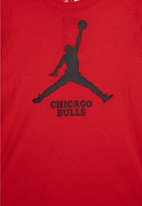 Rød bomull t-skjorte med en svart silhuett av en hoppende figur og teksten "CHICAGO BULLS" i fete svarte bokstaver under.