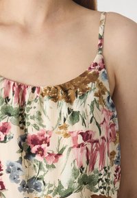 Gros plan d'une femme portant une robe à imprimé floral avec de fines bretelles et un tissu doux froncé au niveau de l'encolure.
