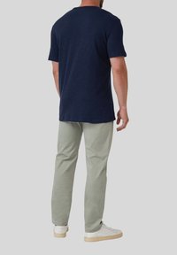 Marineblauw kortef t-shirt, van katoen, relaxed fit, achterkant zichtbaar. Gepaard met lichtgroene broek en witte sneakers. Gladde textuur.