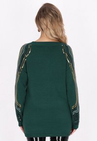 Pulover verde tricotat, cu mâneci lungi și dungi decorative din paiete aurii și negre, croială lejeră și decolteu ribot.