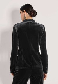 Zwarte fluwelen blazer met een geknipt revers, knoopmanchetten en een getailleerde pasvorm, gezien vanuit de achterkant. Glad textuur met een slanke silhouet.