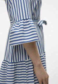 Vestido a rayas en azul y blanco, con mangas acampanadas, cintura ajustada con un lazo y falda de capas. Tela suave y liviana.