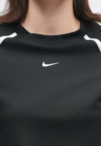 Κοντινό πλάνο ενός ατόμου που φοράει μαύρο αθλητικό μπλουζάκι Nike με λευκό τελείωμα και μικρό λευκό λογότυπο Nike στο κέντρο του στήθους.