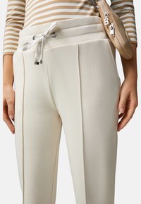 Crème-kleurige broek met een trekkoord in de taille, met twee verticale plooien aan de voorkant en een zachte, gestructureerde stof.