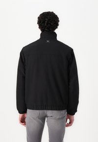 Sort bomberjakke med høj krave, elastiske manchetter og talje. Glat materiale og minimal branding synlig på ryggen.