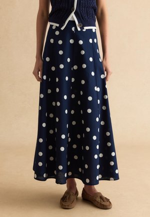 Falda larga azul marino con grandes lunares blancos, combinada con chaleco de punto azul marino y mocasines marrones con borlas.