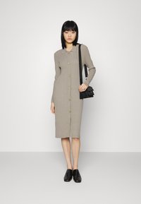 Vestido abotoado, de mangas longas e comprimento médio, na cor cinza mescla, com gola pontuda, textura canelada e botões dourados. Usado com sapatos e bolsa pretos.