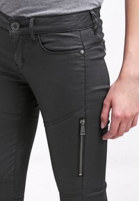 Černé kalhoty z umělé kůže se slim fit střihem, nabízející boční zipovou kapsu, prošívané detaily a hladkou texturu.