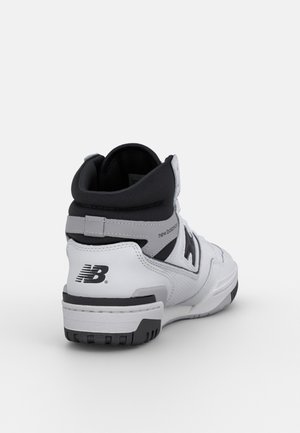 Baskets montantes New Balance blanches et grises vues de dos, montrant un col rembourré noir et un logo sur le talon.