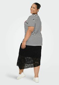 Camiseta de rayas en blanco y negro, combinada con una falda negra de encaje con un patrón floral. La modelo lleva zapatillas blancas.