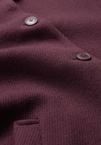 Bordowy materiał o teksturowanej powierzchni z subtelnym prążkowym wzorem. Widać dwa ciemne guziki, które dodają szczegółu projektowi.