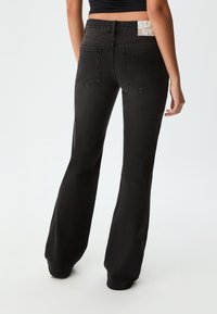 Jeans neri a zampa d'elefante con vita alta, realizzati in denim. Presentano due tasche posteriori e un'etichetta sulla vita.