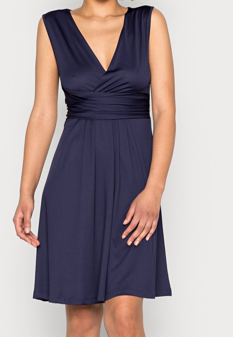 Mörkblå klänning i mjukt, elastiskt tyg. Har en djup V-ringning, är ärmlös och har en samlad midja som flyter ut i en utsvängd kjol.