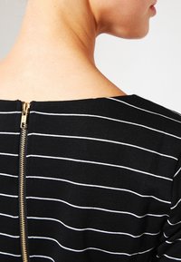 Randig topp i svart och vitt med rundad halsringning, försedd med en guldzipper i ryggen. Mjuk tygkvalitet och slät textur.