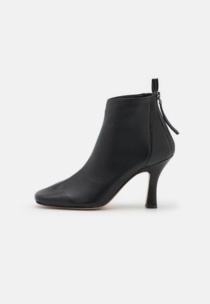 Černá kožená kotníková bota s elegantním designem, špičatou špičkou a úzkým vysokým podpatkem. Obsahuje boční zip pro snadné obouvání.