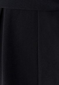 Czarna tkanina o gładkiej, teksturowanej powierzchni z subtelnymi odcieniami. Dopasowany design z czystymi liniami i zagięciami.