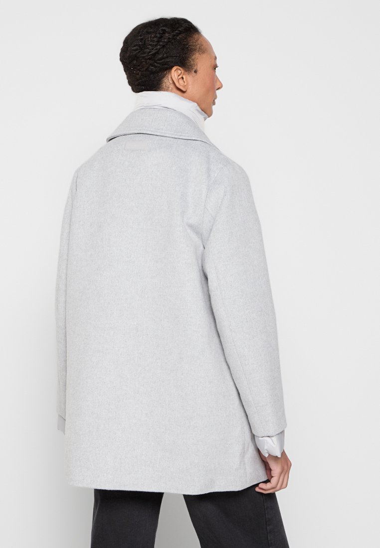 Hellgrauer Wollmantel mit breitem Kragen und geradem Schnitt. Hat lange Ärmel, eine glatte Textur und minimalistischem Stil.