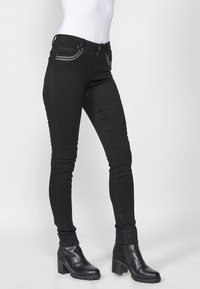 Crne slim-fit traperice s metalnim lancima na džepovima, napravljene od denima. Uparene s crnim čizmama do gležnja s debelim potpeticama.