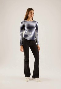 Striped long-sleeve shirt in navy and white, paired with black flared jeans, white sneakers, standing on a neutral background.