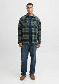 Flanellhemd im grün-blauen Karomuster, mit zwei Brusttaschen und Knopfverschluss, getragen über einem marineblauen Pullover und kombiniert mit blauen Jeans.