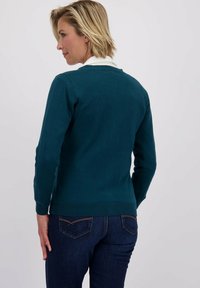 Teal trui met een ronde hals en geribbelde manchetten. Draag het over een witte blouse met kraag, gecombineerd met donkerblauwe jeans. Soepele textuur.