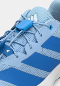 Μπλε αθλητικό παπούτσι με υφή στην επάνω επιφάνεια, που διαθέτει μπλε ρίγες και μπλε κλείδωμα κορδονιών. Επάνω μέρος από ανοιχτό μπλε διχτυωτό υλικό και λευκή σόλα.