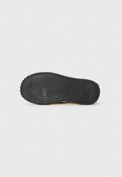 Black rubber shoe sole with a textured surface, featuring a circular accent and patterned tread for grip.