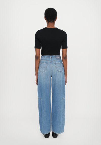 Weitgeschnittene Denim-Jeans in Hellblau mit hoher Taille und mehreren Taschen. Begleitet von einem enganliegenden schwarzen Kurzarmoberteil.