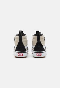 Høytopp sneakers med en kombinasjon av svart og beige semsket skinn, hvit gummisåle og en særegen bakre tab med rødt logo.