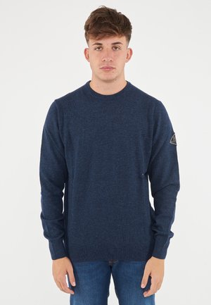 Maglione lavorato a maglia blu navy con scollo rotondo, maniche lunghe e finitura testurizzata. Presenta una toppa con logo sulla manica sinistra.