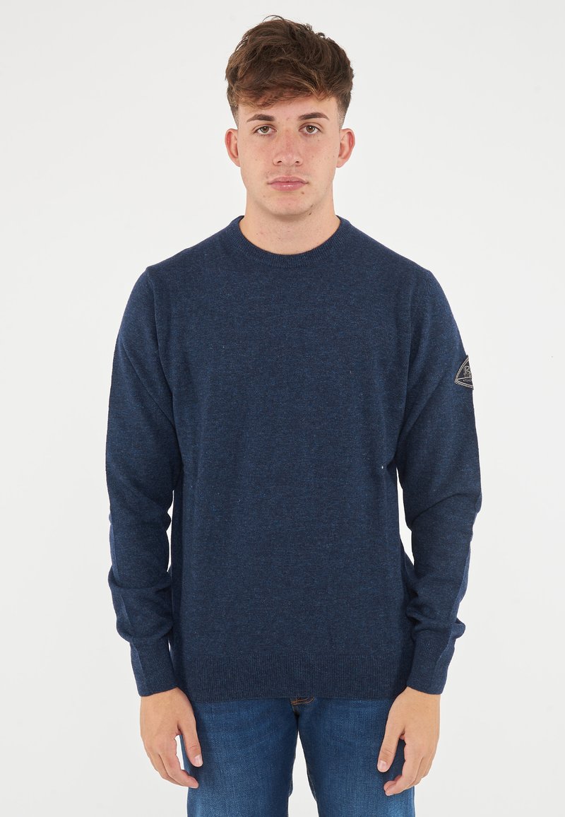 Maglione lavorato a maglia blu navy con scollo rotondo, maniche lunghe e finitura testurizzata. Presenta una toppa con logo sulla manica sinistra.
