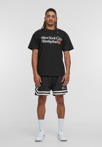 Sort bomulds T-shirt med teksten "New York City Basketball", parret med sorte mesh shorts med hvide detaljer. Hvide sneakers og sokker.