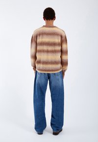 Brun och krämrandig tröja i fluffigt material, tillsammans med löst sittande blå denimjeans. Synlig sömnad och stora manschetter.