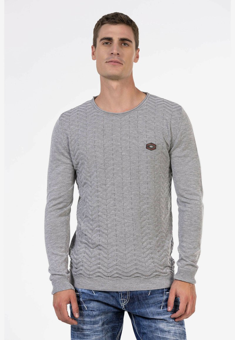 Grauer Strickpullover mit einem strukturierten Zickzackmuster, rundem Ausschnitt und gerippten Bündchen. Kleines Logopatch sichtbar auf der Brust.