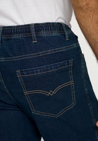 Jeans de mezclilla azul oscuro con una cinturilla ancha, bolsillos traseros con un diseño de costura distintivo y una textura suave.