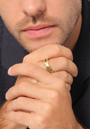 Guldring med indvævede bånd, mat og poleret finish. Hænder samlet, med en struktureret baggrund og neutrale hudtoner.