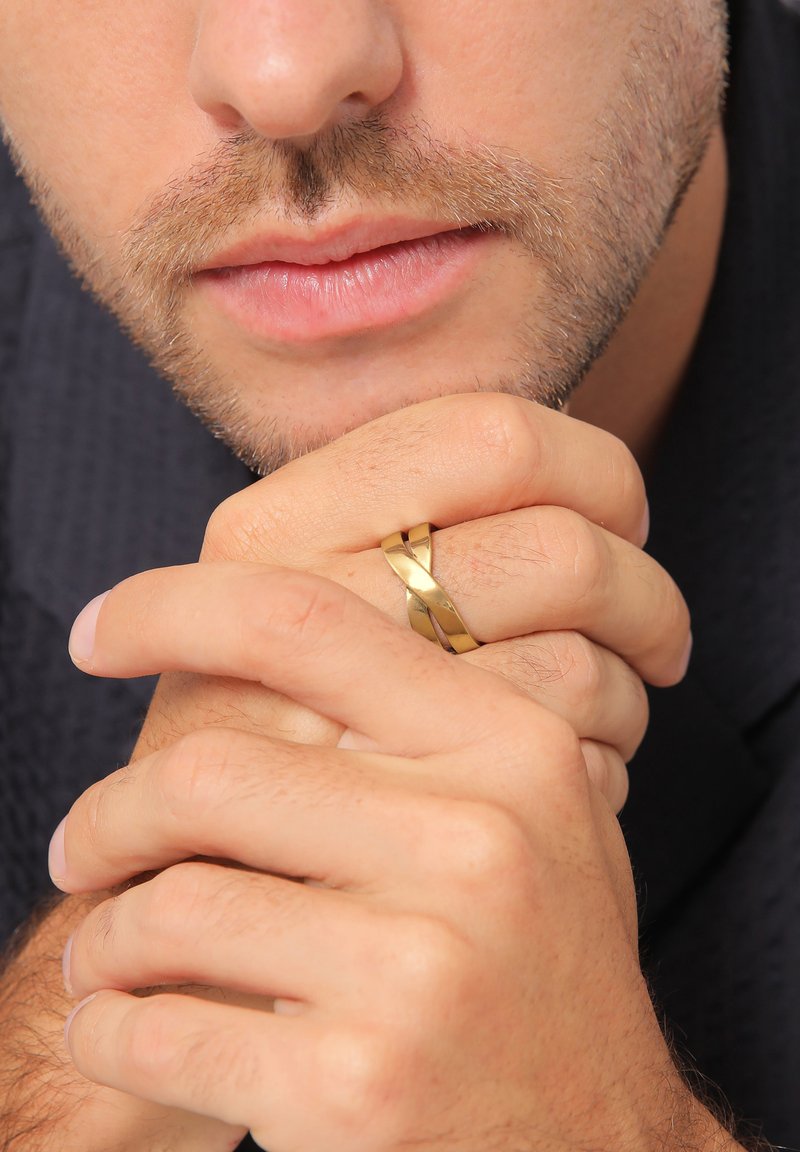 Guldring med indvævede bånd, mat og poleret finish. Hænder samlet, med en struktureret baggrund og neutrale hudtoner.