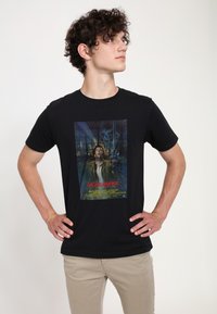 Černé bavlněné tričko s barevnou grafikou filmu "Highlander", obsahující postavu se mečem na pozadí s lebkou.