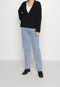 Antracytowy sweter rozpinany na guziki z dekoltem w serek, długimi rękawami, w połączeniu z jasnoniebieskimi prostymi jeansami i czarnymi botkami na obcasie.
