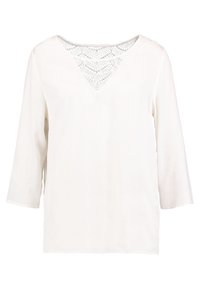 Blouse blanche à manches trois-quarts, col en V avec détail en dentelle motif losange, tissu lisse et coupe décontractée.